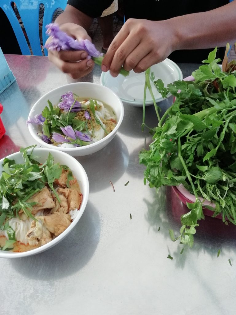 garnishing a bowl of num banh chok on our Phnom Penh food crawl